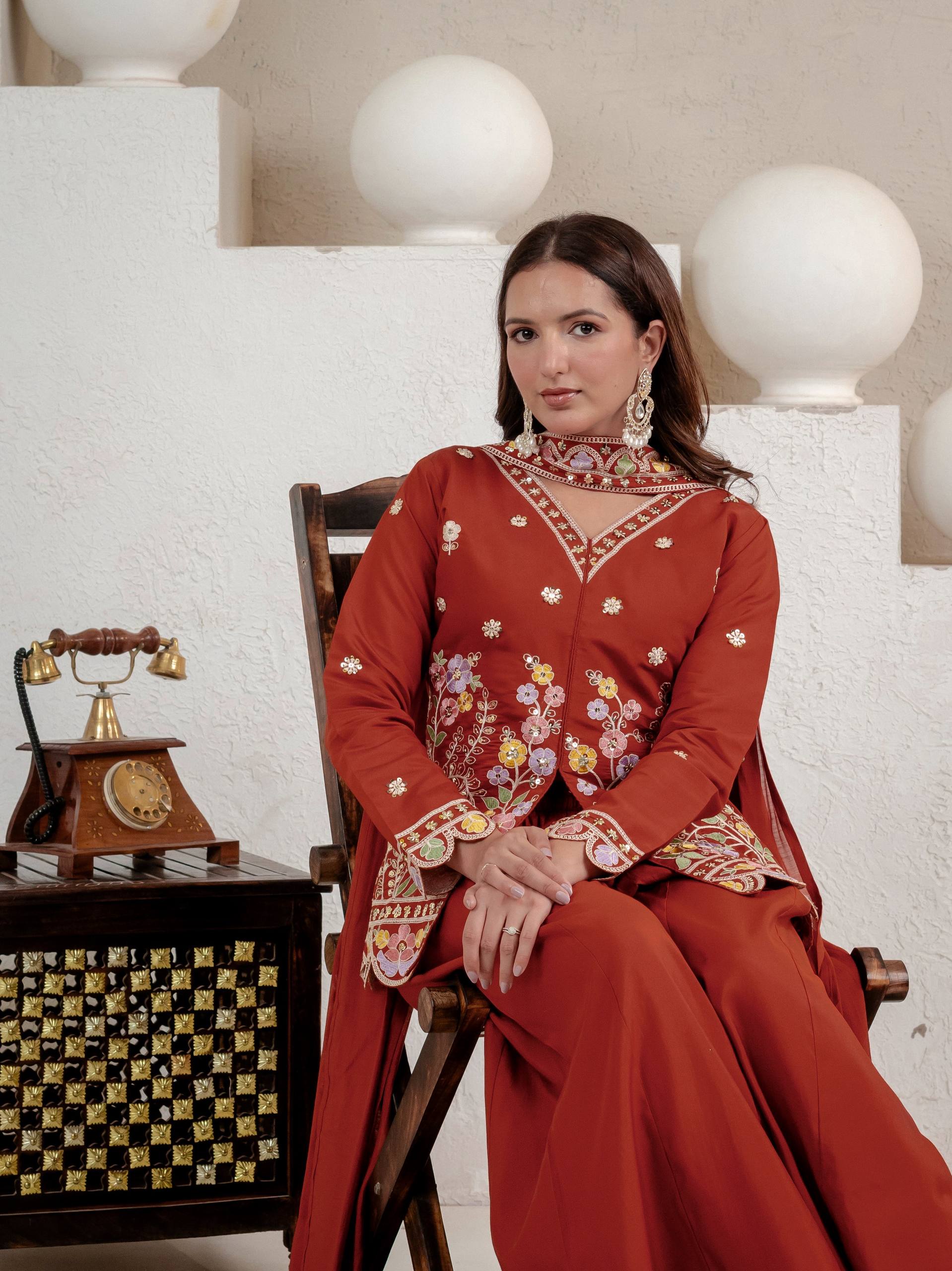 Resplendent Rust Orange Peplum Kurti and Flared Palazzo Suit Set Adorned with Intricate Multicolored Floral Embroidery, Sequin Accents, and Ornate Scalloped Borders